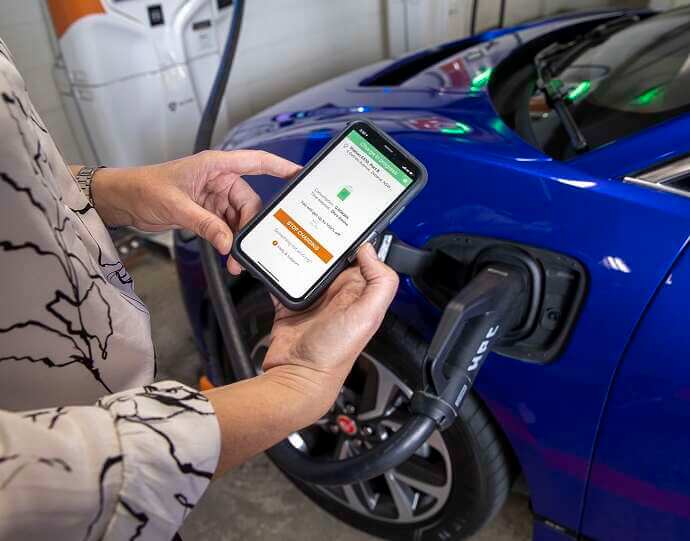 electric car charging with lady holding mobile phone showing app 176376